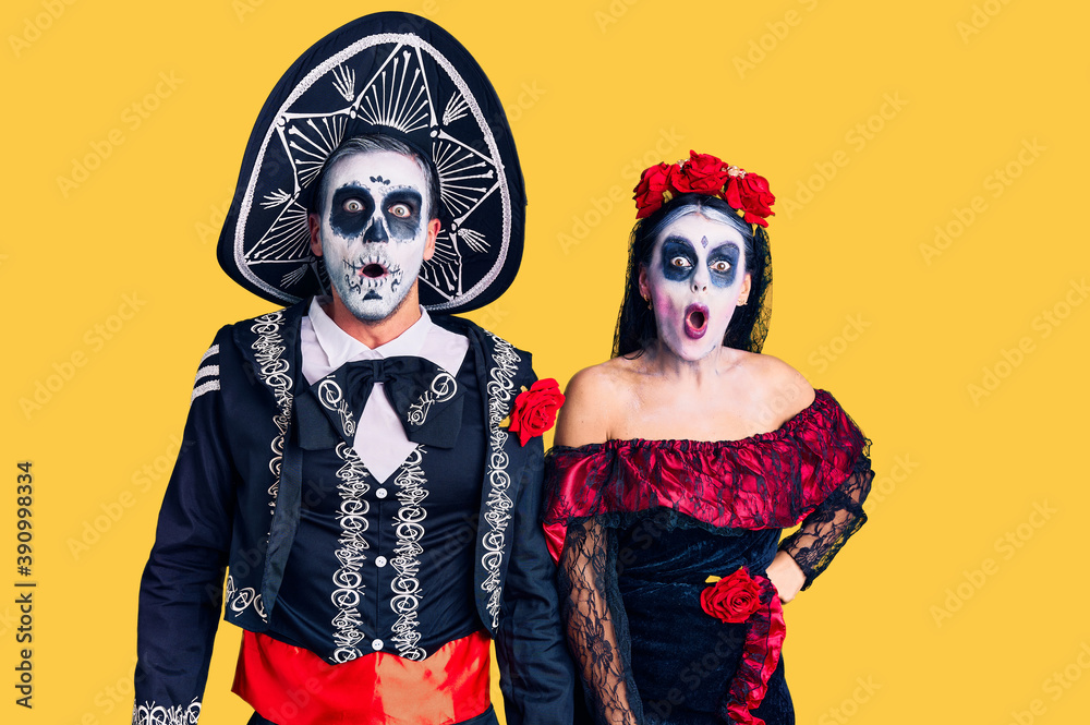 Young couple wearing mexican day of the dead costume over background afraid and shocked with surprise and amazed expression, fear and excited face.