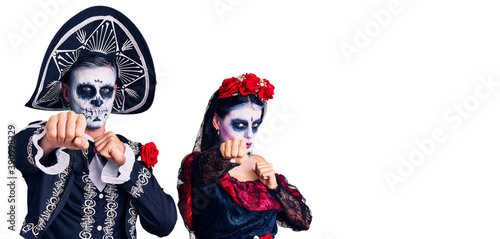 Young couple wearing mexican day of the dead costume over background punching fist to fight, aggressive and angry attack, threat and violence