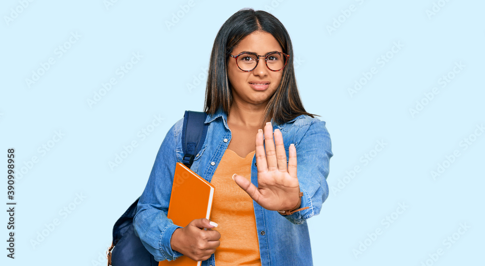 Young latin girl wearing student backpack and holding books doing stop gesture with hands palms, angry and frustration expression Young latin girl wearing student backpack and holding books doing stop gesture with hands palms, angry and frustration expression
