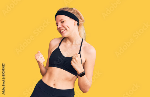 Young beautiful blonde woman wearing sportswear very happy and excited doing winner gesture with arms raised, smiling and screaming for success. celebration concept.