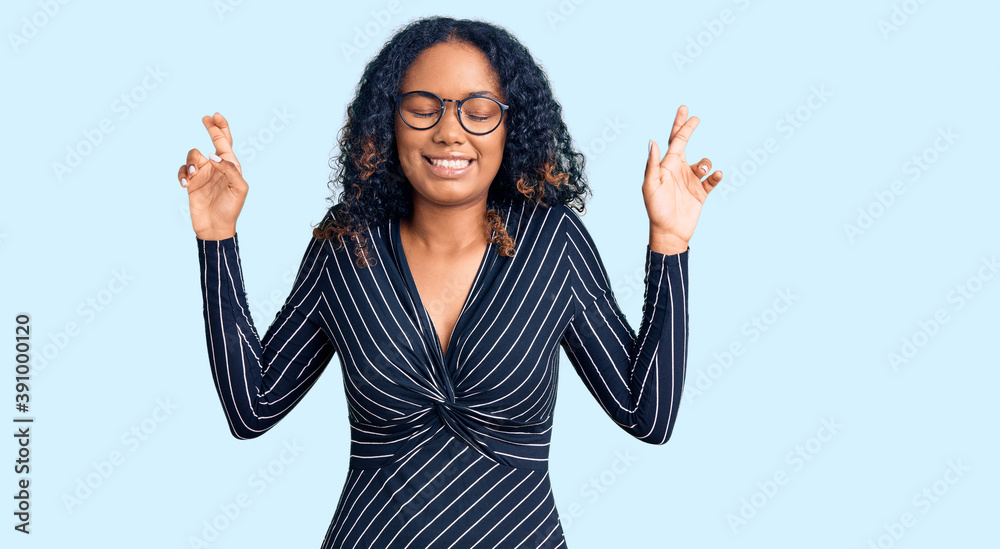 Young african american woman wearing casual clothes and glasses gesturing finger crossed smiling with hope and eyes closed. luck and superstitious concept. Young african american woman wearing casual clothes and glasses gesturing finger crossed smiling with hope and eyes closed. luck and superstitious concept.
