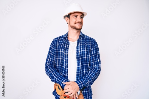 Young handsome man weaing handyman uniform looking away to side with smile on face, natural expression. laughing confident. photo