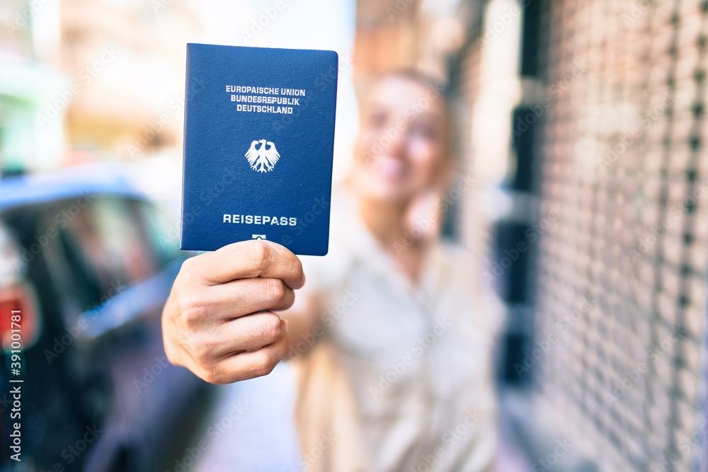 Young beautiful blonde caucasian woman smiling happy outdoors on a sunny day showing Germany passport