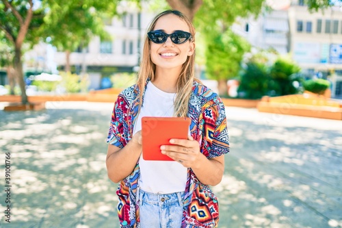 Young beautiful blonde caucasian woman smiling happy outdoors on a sunny day using touchpad device photo