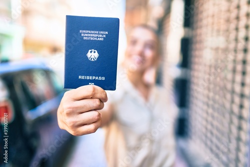Young beautiful blonde caucasian woman smiling happy outdoors on a sunny day showing Germany passport