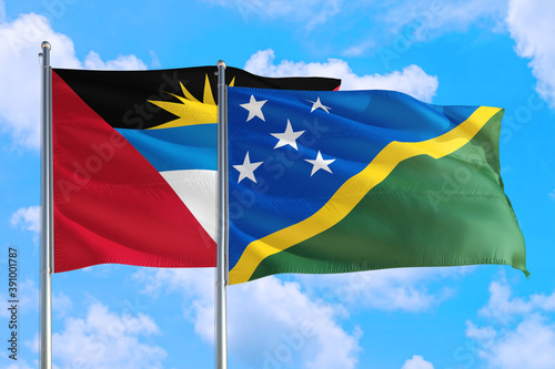 Solomon Islands and Antigua and Barbuda national flag waving in the windy deep blue sky. Diplomacy and international relations concept.