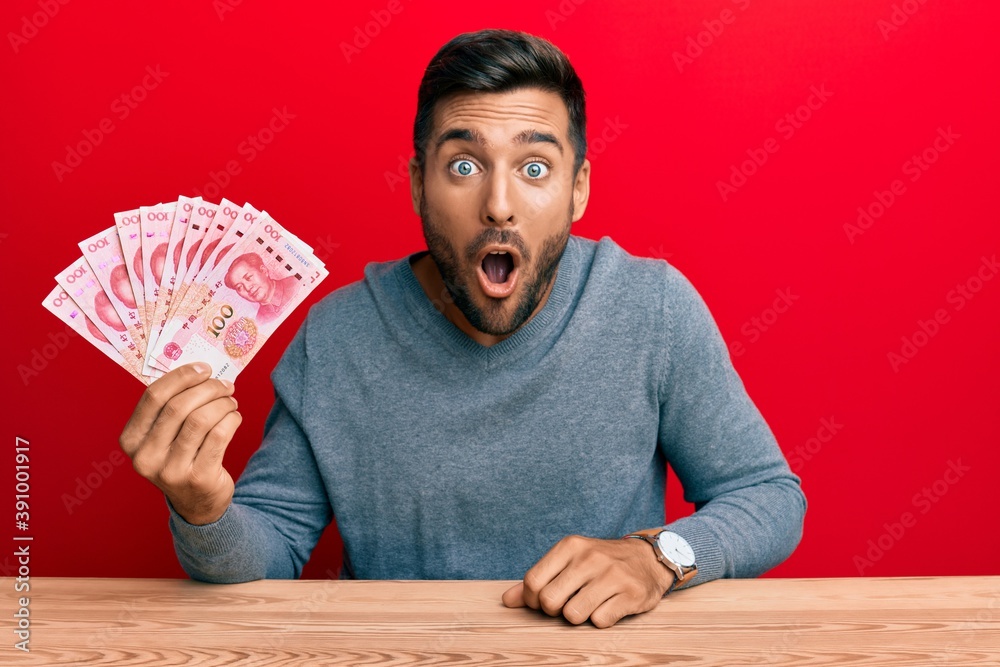 Handsome hispanic man holding yuan chinese banknotes scared and amazed with open mouth for surprise, disbelief face Handsome hispanic man holding yuan chinese banknotes scared and amazed with open mouth for surprise, disbelief face