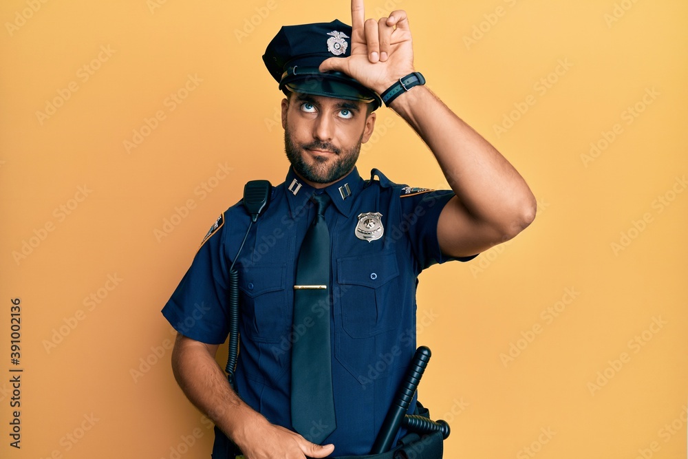 Handsome hispanic man wearing police uniform making fun of people with fingers on forehead doing loser gesture mocking and insulting.