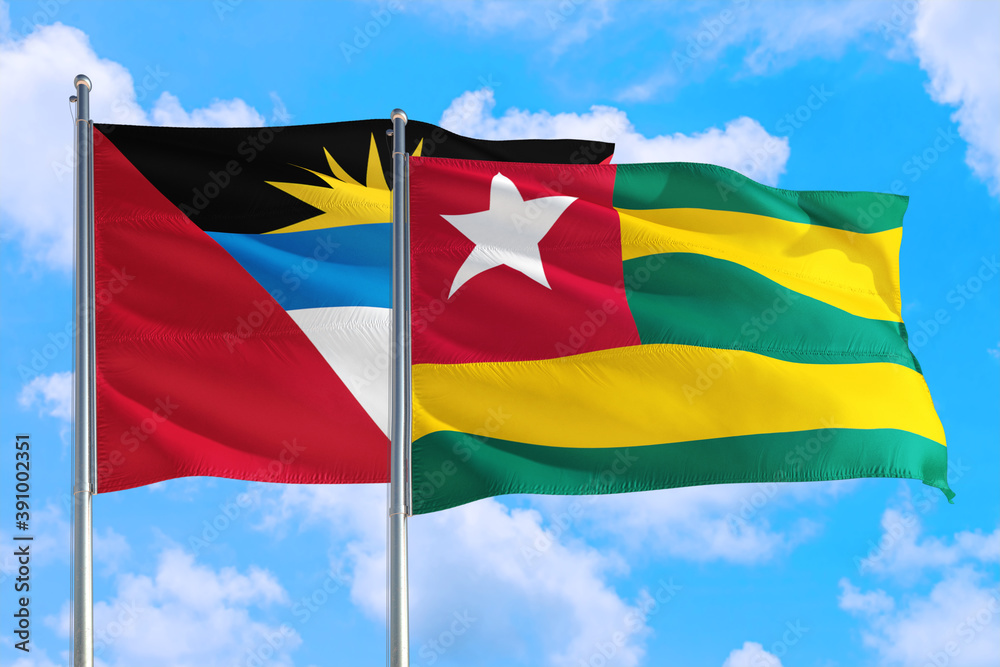 Togo and Antigua and Barbuda national flag waving in the windy deep blue sky. Diplomacy and international relations concept. Togo and Antigua and Barbuda national flag waving in the windy deep blue sky. Diplomacy and international relations concept.