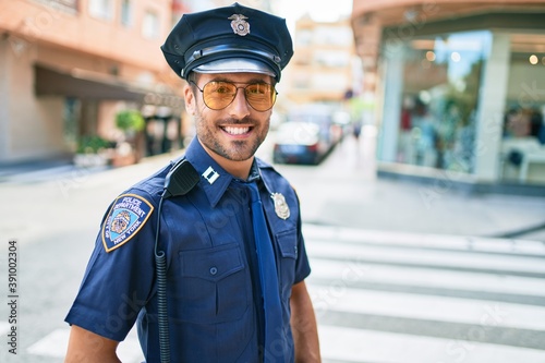 Fotografering Young handsome hispanic policeman wearing police uniform smiling happy Standing with smile on face at town street