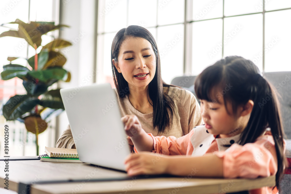 Mother and asian kid little girl learning and looking at laptop computer making homework studying knowledge with online education e-learning system.children video conference with teacher tutor at home Mother and asian kid little girl learning and looking at laptop computer making homework studying knowledge with online education e-learning system.children video conference with teacher tutor at home