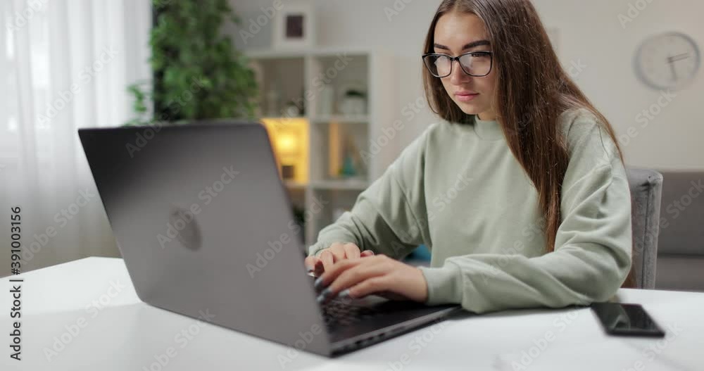Confident young woman in eyeglasses working on portable computer while staying at home. Concept of people, technology and remote work. Confident young woman in eyeglasses working on portable computer while staying at home. Concept of people, technology and remote work.