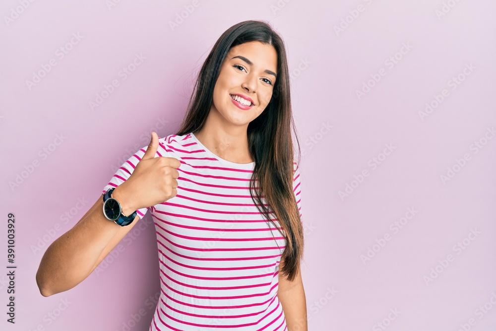 Young brunette woman wearing casual clothes over pink background doing happy thumbs up gesture with hand. approving expression looking at the camera showing success. Young brunette woman wearing casual clothes over pink background doing happy thumbs up gesture with hand. approving expression looking at the camera showing success.