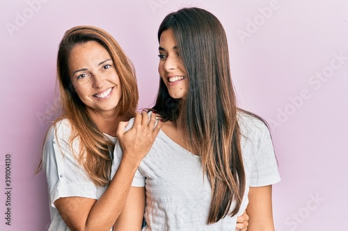 Beautiful hispanic mother and daughter smiling happy hugging over isolated pink background.