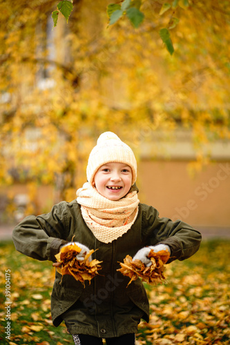 girl in a green jacket  yellow hat and scarf plays in the autumn park. cheerful joyful child playing with autumn leaves in the park. a great start to the golden autumn. 