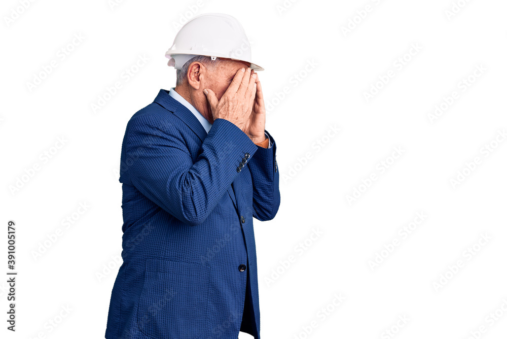 Senior handsome grey-haired man wearing suit and architect hardhat with sad expression covering face with hands while crying. depression concept. Senior handsome grey-haired man wearing suit and architect hardhat with sad expression covering face with hands while crying. depression concept.