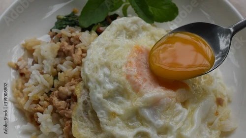 spoon scooping egg yolk topping spicy fried chop pork with basilleaf and chili on rice in dish photo