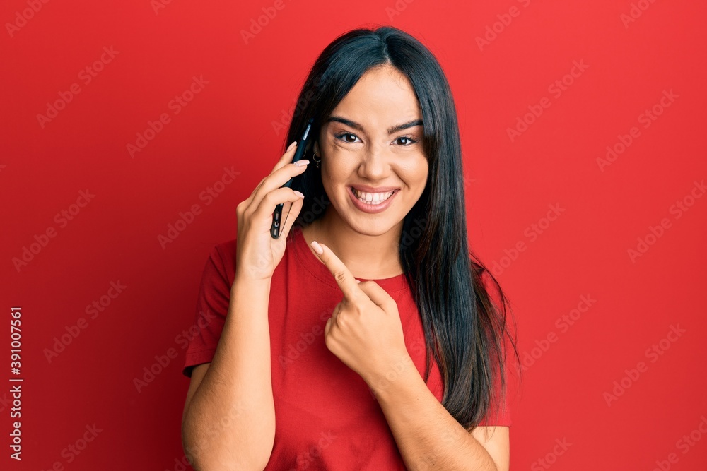 Young beautiful hispanic girl having conversation talking on the smartphone smiling happy pointing with hand and finger Young beautiful hispanic girl having conversation talking on the smartphone smiling happy pointing with hand and finger