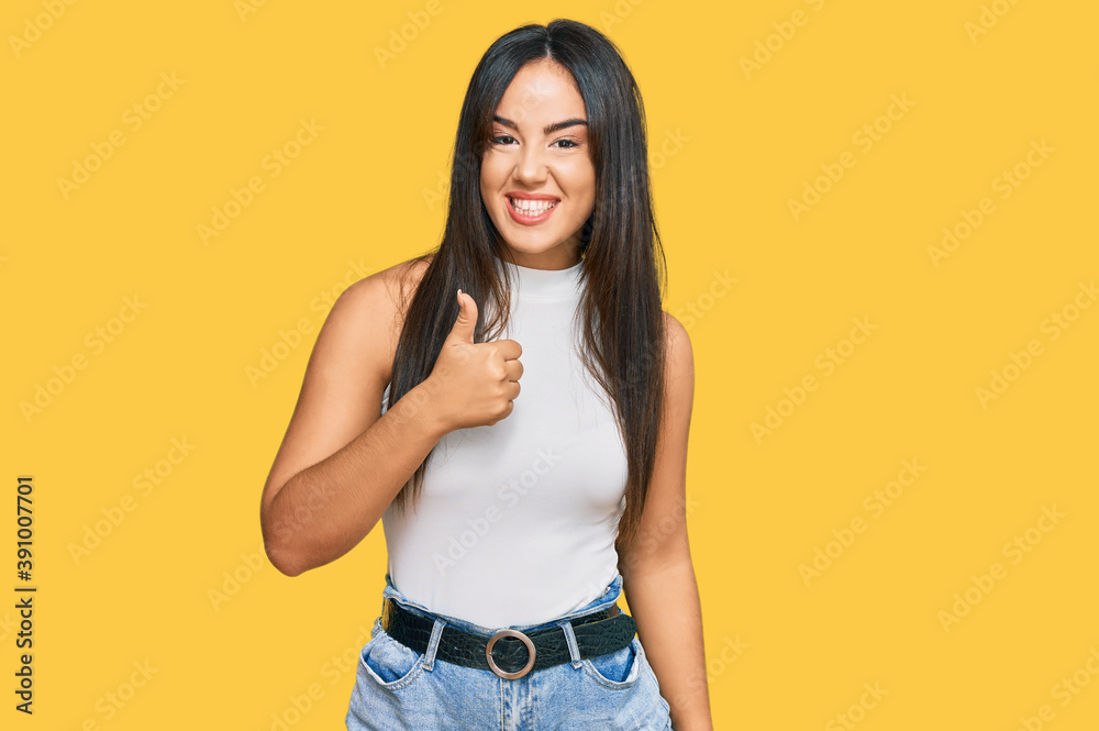 Young beautiful hispanic girl wearing casual clothes doing happy thumbs up gesture with hand. approving expression looking at the camera showing success. Young beautiful hispanic girl wearing casual clothes doing happy thumbs up gesture with hand. approving expression looking at the camera showing success.