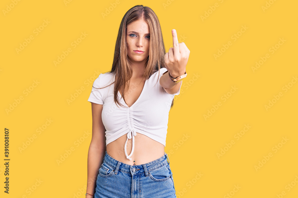 Young beautiful blonde woman wearing casual white tshirt showing middle finger, impolite and rude fuck off expression Young beautiful blonde woman wearing casual white tshirt showing middle finger, impolite and rude fuck off expression