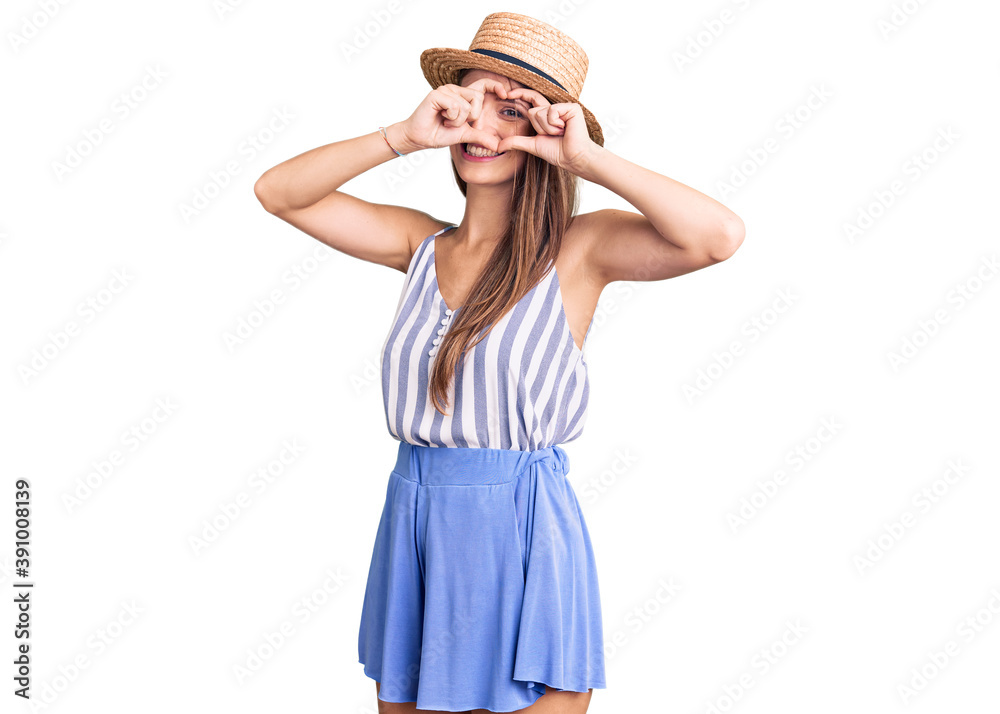 Young beautiful blonde woman wearing summer hat doing heart shape with hand and fingers smiling looking through sign Young beautiful blonde woman wearing summer hat doing heart shape with hand and fingers smiling looking through sign
