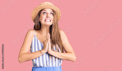 Young beautiful blonde woman wearing summer hat begging and praying with hands together with hope expression on face very emotional and worried. begging.