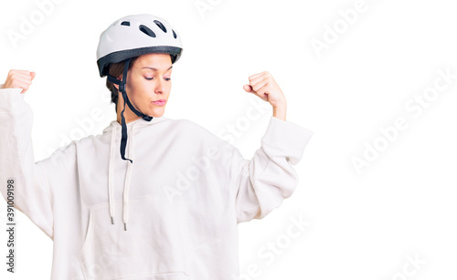 Beautiful brunette young woman wearing bike helmet and sporty clothes showing arms muscles smiling proud. fitness concept. © Krakenimages.com