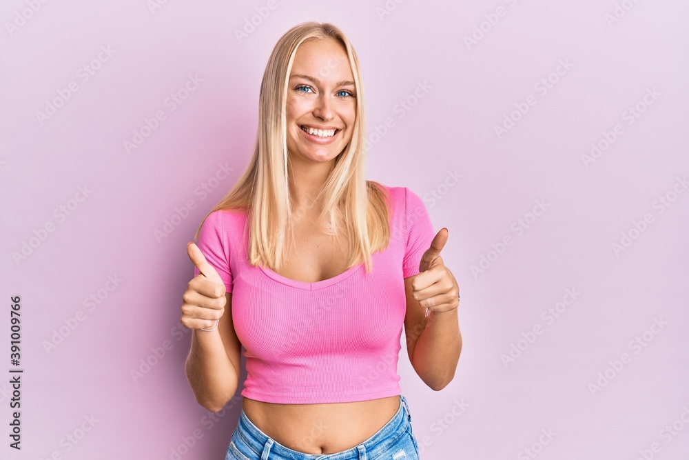Young blonde girl wearing casual clothes success sign doing positive gesture with hand, thumbs up smiling and happy. cheerful expression and winner gesture. Young blonde girl wearing casual clothes success sign doing positive gesture with hand, thumbs up smiling and happy. cheerful expression and winner gesture.