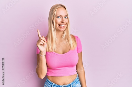 Young blonde girl wearing casual clothes showing and pointing up with finger number one while smiling confident and happy. © Krakenimages.com