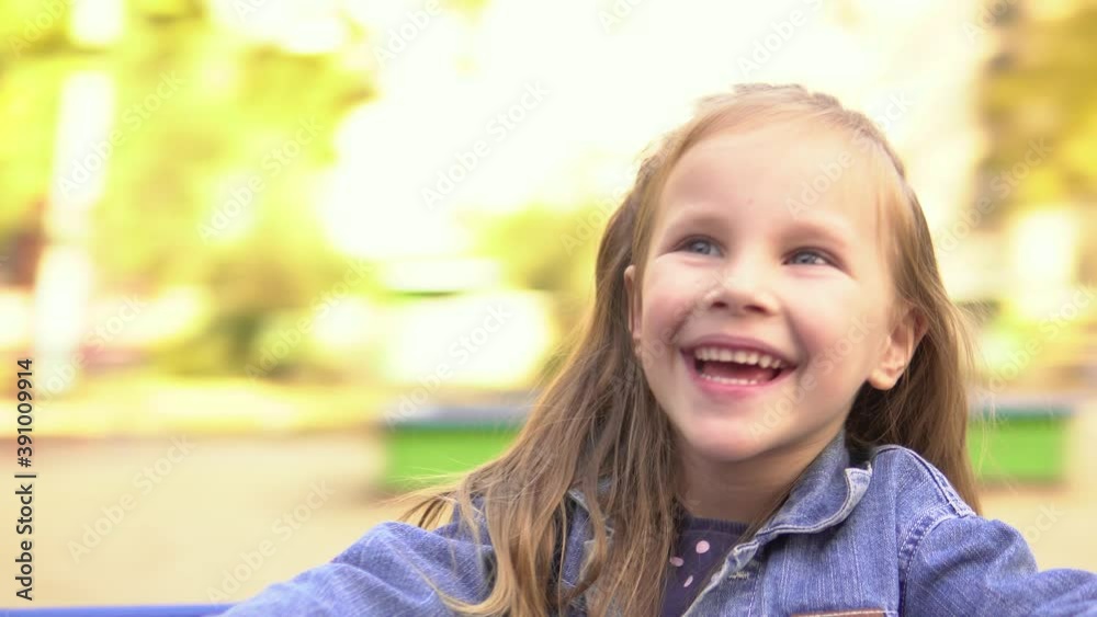 Little beautiful girl is spinning on the carousel looking at the camera and smiling happily.Playground. Little beautiful girl is spinning on the carousel looking at the camera and smiling happily.Playground.
