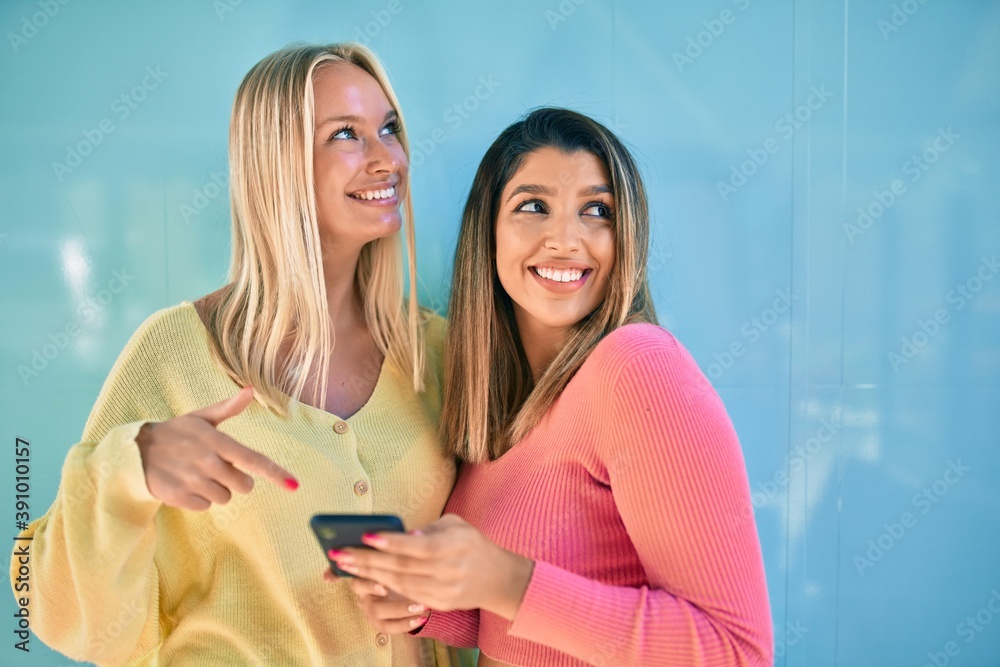 Two beautiful and young girl friends together having fun at the city using smartphone Two beautiful and young girl friends together having fun at the city using smartphone