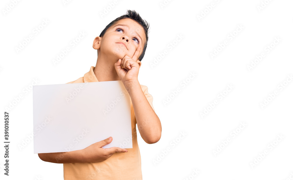 Little cute boy kid holding cardboard banner with blank space serious face thinking about question with hand on chin, thoughtful about confusing idea Little cute boy kid holding cardboard banner with blank space serious face thinking about question with hand on chin, thoughtful about confusing idea