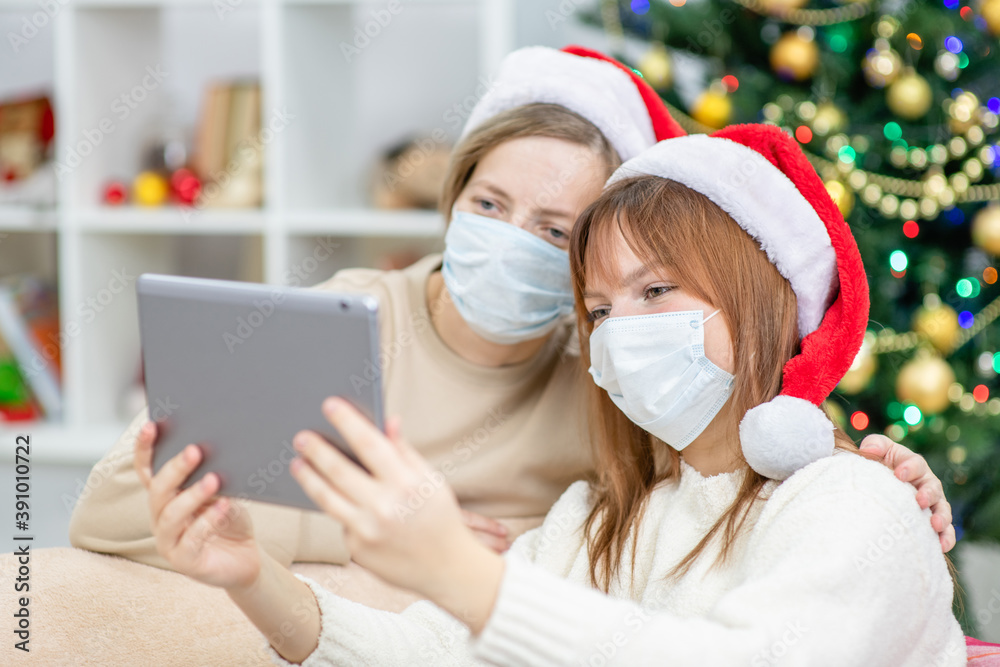 Happy family wearing Christmas hats, take video calls during coronavirus pandemic, with Christmas tree on the background. Coronavirus and Christmas concept