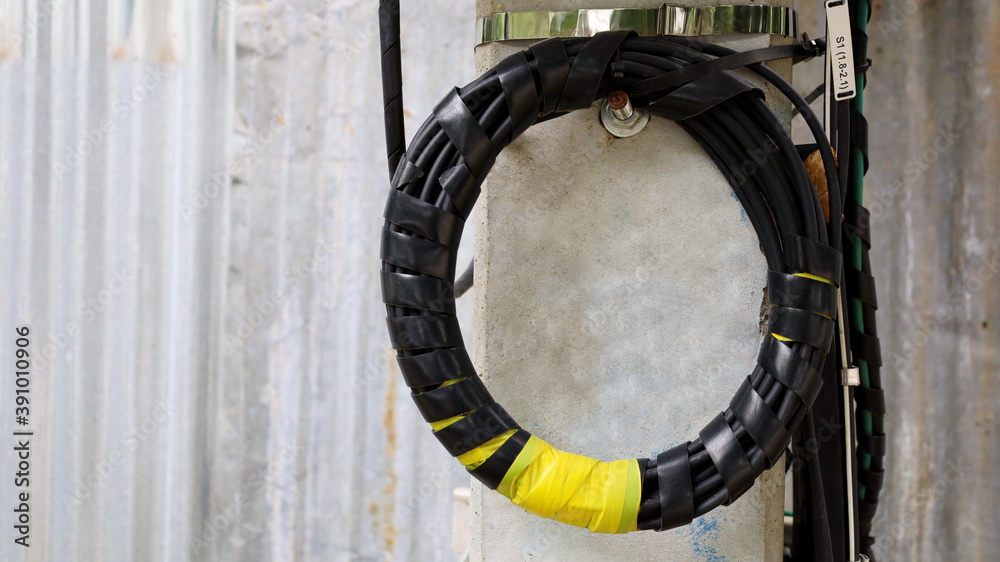 A roll of fiber-optic cables hanging from a pole. Optical fiber cable of high speed internet communication On the background of a galvanized wall with a copy area. Close focus and select an object