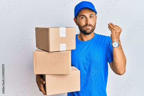 Handsome man with beard wearing courier uniform holding delivery packages doing italian gesture with hand and fingers confident expression © Krakenimages.com