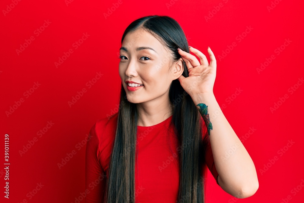 Young chinese woman wearing casual clothes smiling with hand over ear listening and hearing to rumor or gossip. deafness concept. Young chinese woman wearing casual clothes smiling with hand over ear listening and hearing to rumor or gossip. deafness concept.