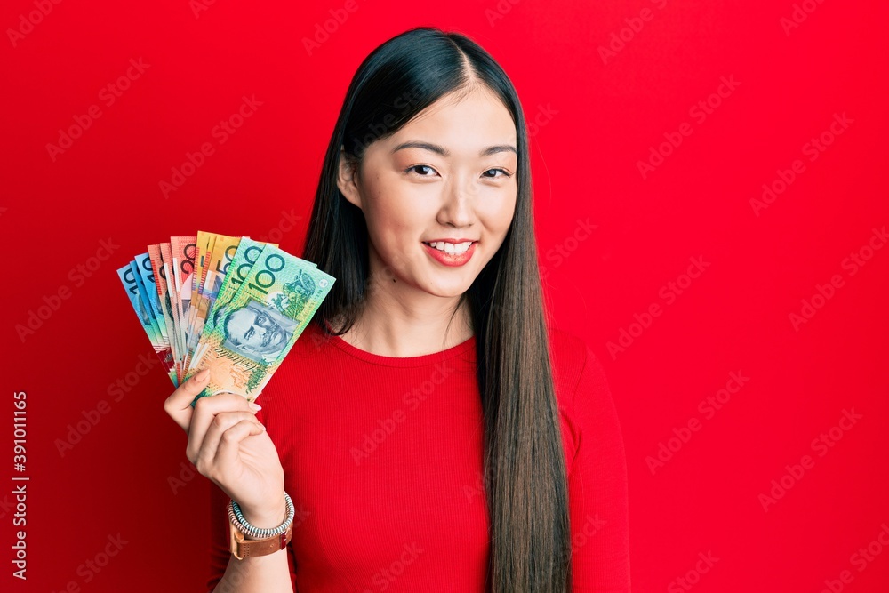 Young chinese woman holding australian dollars looking positive and happy standing and smiling with a confident smile showing teeth Young chinese woman holding australian dollars looking positive and happy standing and smiling with a confident smile showing teeth