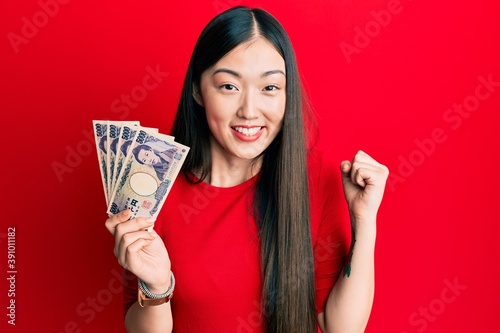 Fotografía Young chinese woman holding japanese yen banknotes screaming proud, celebrating