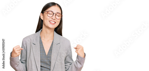 Young chinese woman wearing business clothes very happy and excited doing winner gesture with arms raised, smiling and screaming for success. celebration concept.