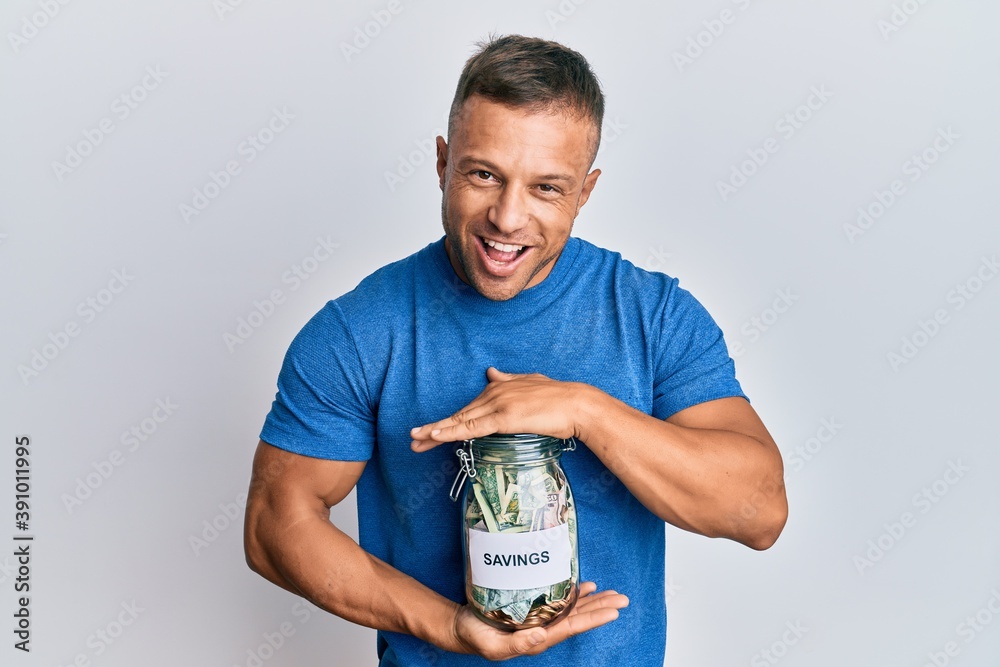 Handsome muscle man holding jar with savings smiling and laughing hard out loud because funny crazy joke. Handsome muscle man holding jar with savings smiling and laughing hard out loud because funny crazy joke.
