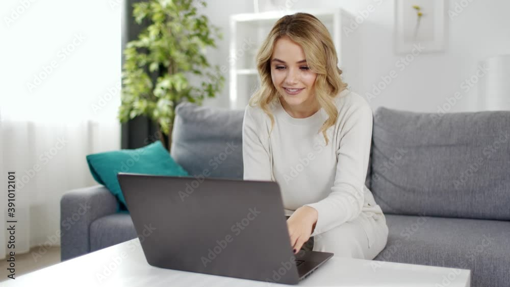 Happy blonde female in casual clothing relaxing on comfortable couch and chatting with friends using wireless laptop. Convenience from modern technologies. Happy blonde female in casual clothing relaxing on comfortable couch and chatting with friends using wireless laptop. Convenience from modern technologies.