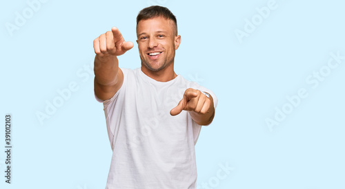 Handsome muscle man wearing casual white tshirt pointing to you and the camera with fingers, smiling positive and cheerful