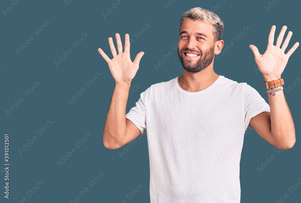 Young handsome blond man wearing casual t-shirt showing and pointing up with fingers number ten while smiling confident and happy.