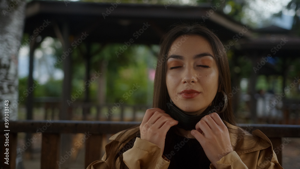 Beautiful woman wearing black mask, sitting on a bench during pandemic period and she is taking off her mask and breathing and smiling while looking at camera, lifestyle and pandemic covid-19 Beautiful woman wearing black mask, sitting on a bench during pandemic period and she is taking off her mask and breathing and smiling while looking at camera, lifestyle and pandemic covid-19
