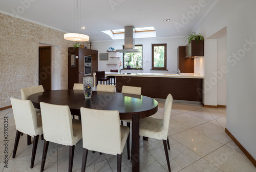 Modern spacious interior of kitchen. Wooden kitchen set with white counter. Roof window. Table and chairs.