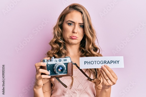 Young blonde girl holding vintage camera and paper with photography word paper depressed and worry for distress, crying angry and afraid. sad expression.