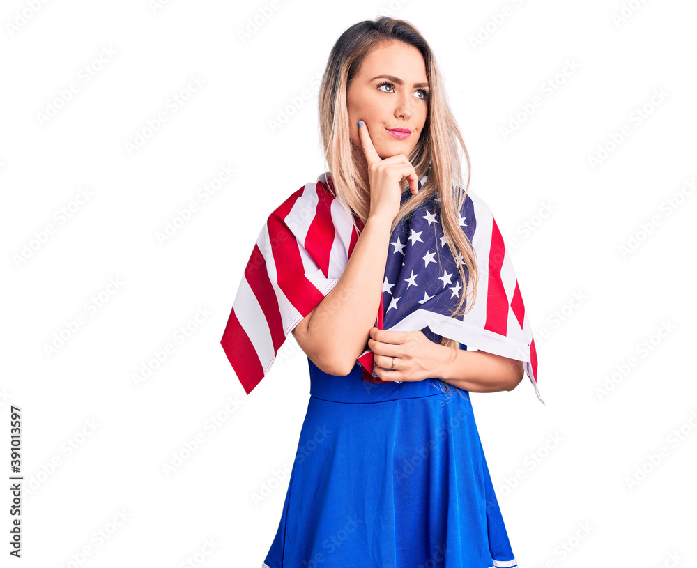 Naklejka premium Young beautiful blonde woman wearing cheerleader uniform and united states flag serious face thinking about question with hand on chin, thoughtful about confusing idea
