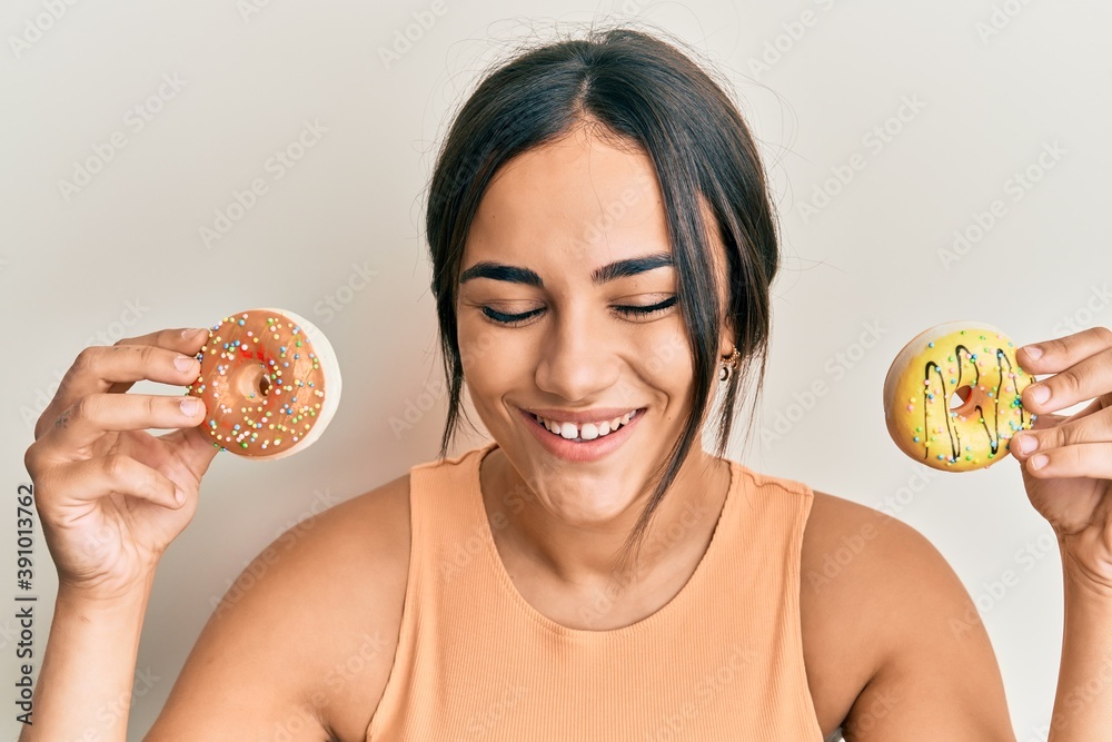 Young brunette woman holding tasty colorful doughnuts smiling and laughing hard out loud because funny crazy joke. Young brunette woman holding tasty colorful doughnuts smiling and laughing hard out loud because funny crazy joke.