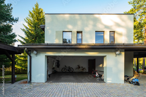 Exterior of luxury private house at sunny summer day. Green pines. Bicycles and children's cars in the garage. photo