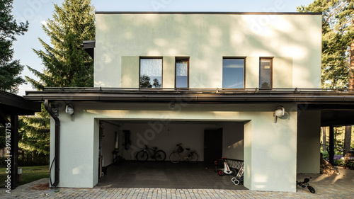 Exterior of luxury private house at sunny summer day. Green pines. Bicycles and children s cars in the garage.